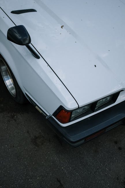 Close-up shot of a vintage white car's hood featuring a classic design with side mirror and headlight.